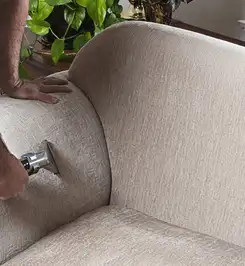 Professional upholstery cleaner deep-cleaning a fabric sofa with a handheld extraction tool and hose Naperville, IL.