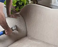 Professional upholstery cleaner deep-cleaning a fabric sofa with a handheld extraction tool and hose in Naperville, IL.